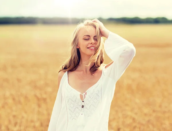 Lächelnde junge Frau im weißen Kleid auf einem Getreidefeld — Stockfoto