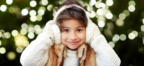 Happy little girl in earmuffs over winter forest — Stock Photo, Image