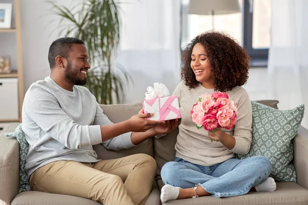 Szczęśliwa para z kwiatami i prezentem w domu — Zdjęcie stockowe