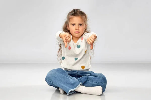 Smutna dziewczyna siedzi na podłodze i pokazuje kciuki w dół — Zdjęcie stockowe