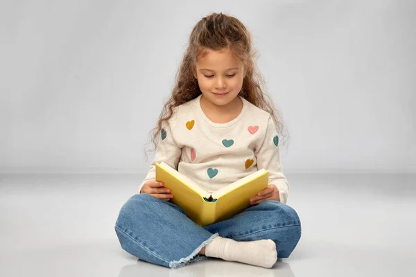 Bela menina sorridente leitura livro no chão — Fotografia de Stock