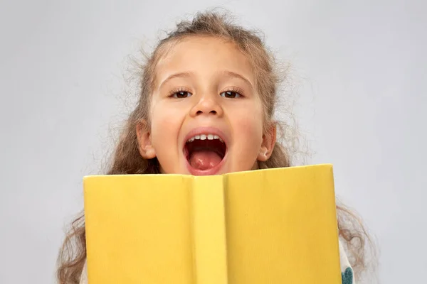 Menina feliz escondendo atrás do livro amarelo — Fotografia de Stock
