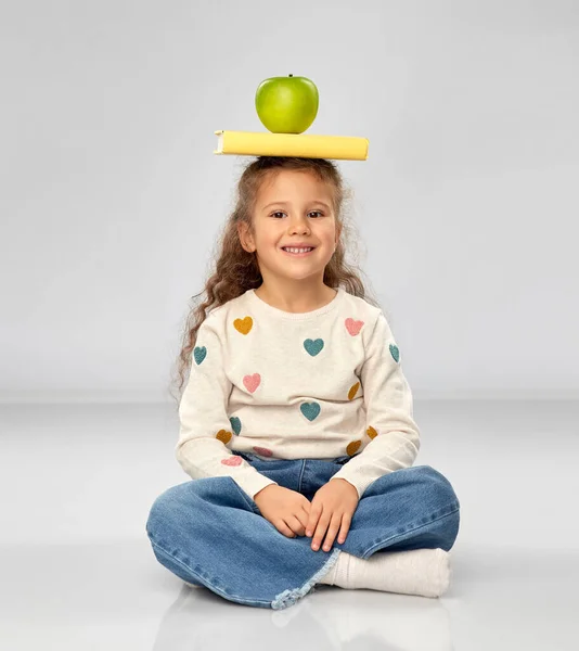 Маленькая девочка с книгой и яблоком сидит на полу — стоковое фото