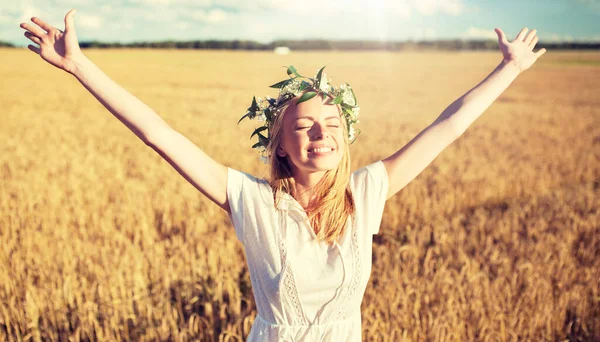 Glückliche junge Frau im Blumenkranz auf einem Getreidefeld — Stockfoto