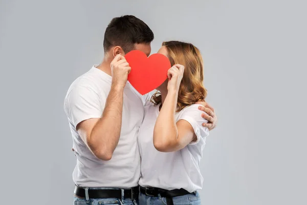 Sonriente pareja besándose detrás de grande rojo corazón — Foto de Stock