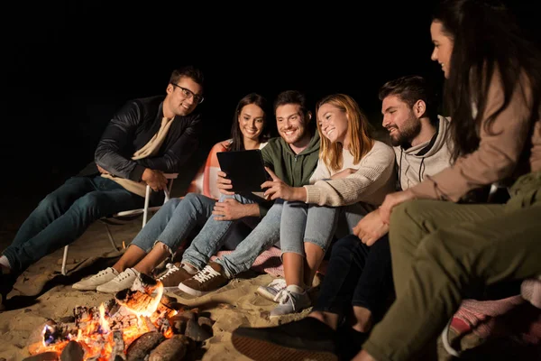 Amis avec tablette PC au feu sur la plage la nuit — Photo