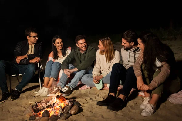 Sekelompok teman duduk di kamp api di pantai — Stok Foto