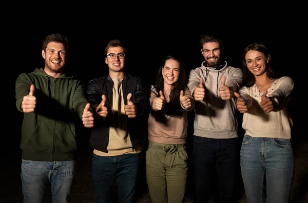 Happy smiling friends showing thumbs up at night — Stock Photo, Image