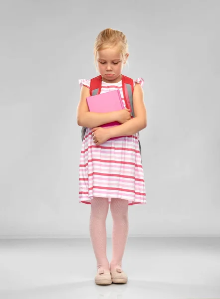 Triste niña estudiante con la bolsa de la escuela y libro — Foto de Stock