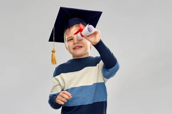 Little boy in mortarboard looking through diploma — Stock Photo, Image