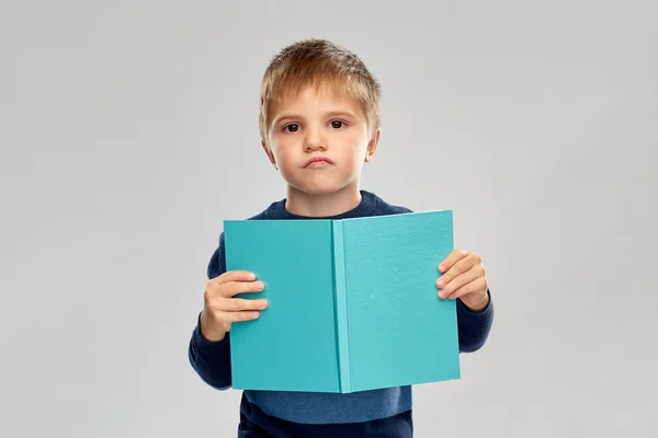 Unpleased little boy reading book — стоковое фото