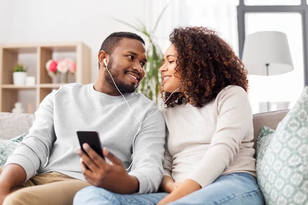 Casal feliz com smartphone e fones de ouvido em casa — Fotografia de Stock