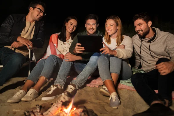 Przyjaciele z tabletem przy ognisku na plaży w nocy — Zdjęcie stockowe