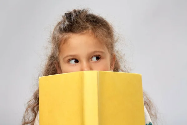 Menina se escondendo atrás do livro amarelo — Fotografia de Stock