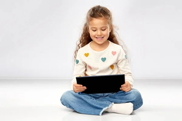 Tablet bilgisayarlı gülümseyen kız yerde oturuyor. — Stok fotoğraf