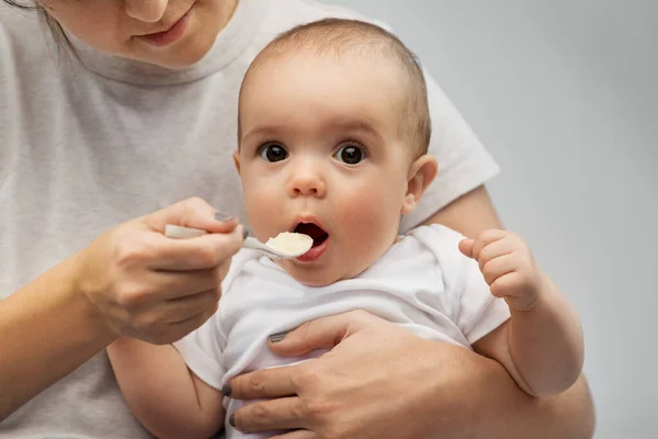 Close up de mãe com colher alimentando pequeno bebê — Fotografia de Stock