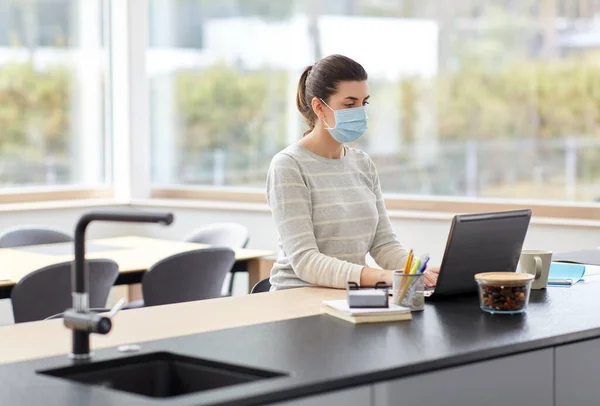 Mujer en la máscara con el ordenador portátil de trabajo en casa oficina — Foto de Stock