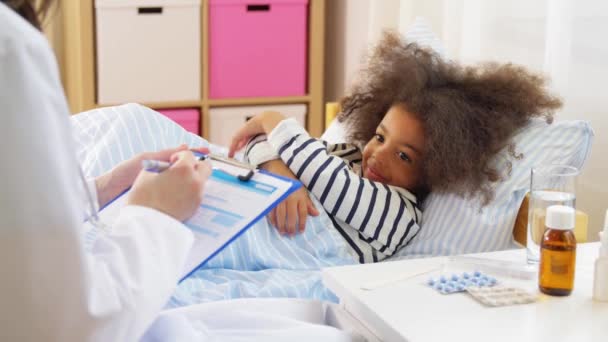 Doctor with clipboard and sick girl in bed at home — Stock Video