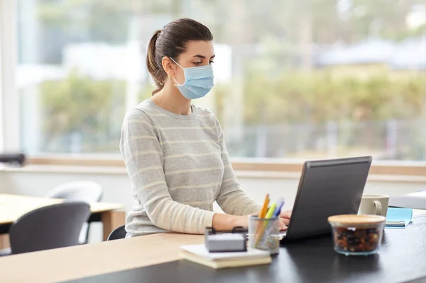 Kobieta w masce z laptopem pracująca w biurze — Zdjęcie stockowe