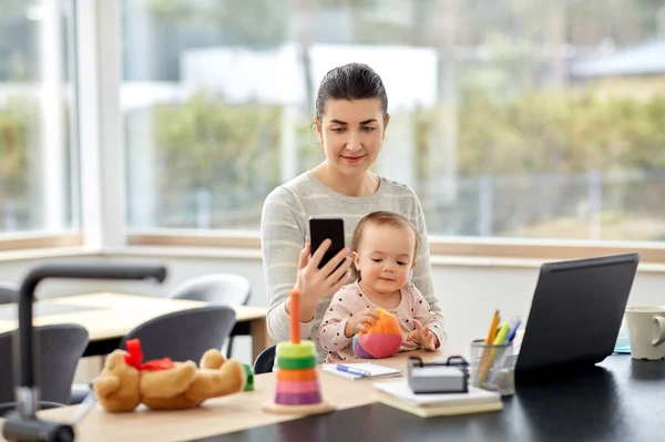 Мати з дитиною і телефоном працює в домашньому офісі — стокове фото