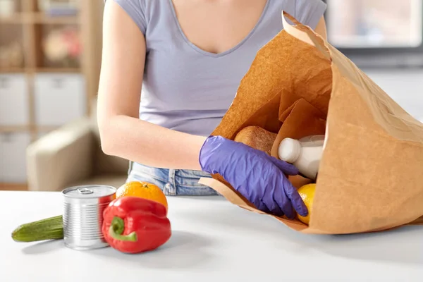 Vrouw in handschoenen het nemen van voedsel uit papieren zak thuis — Stockfoto