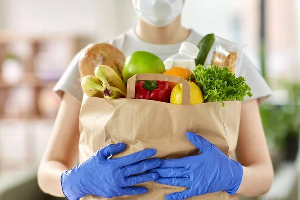 Mujer en guantes con comida en bolsa de papel en casa —  Fotos de Stock