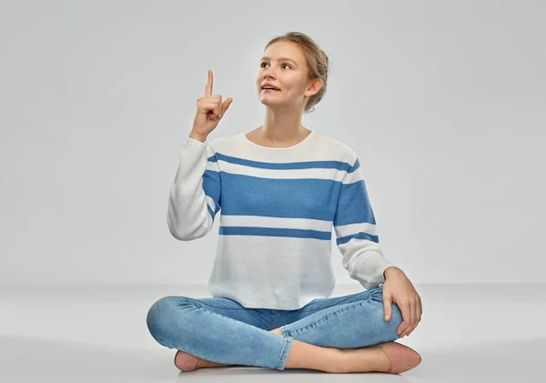 Adolescente apuntando el dedo hacia arriba sentado en el suelo — Foto de Stock