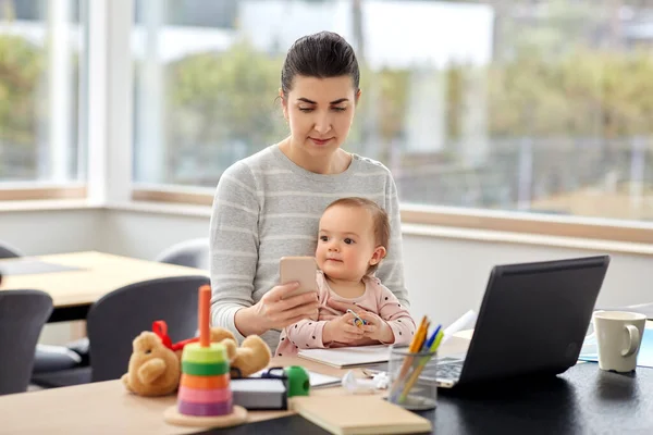 Madre con el bebé y el teléfono trabajando en la oficina en casa — Foto de Stock
