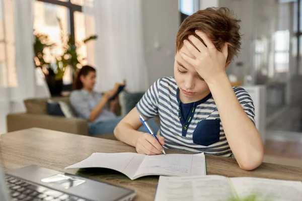 Student chlapec s knihou psaní do notebooku doma — Stock fotografie