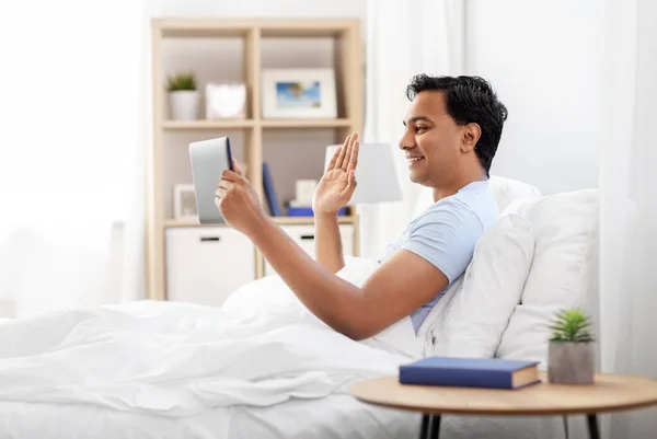 Hombre feliz con la tableta PC en la cama teniendo videollamada —  Fotos de Stock