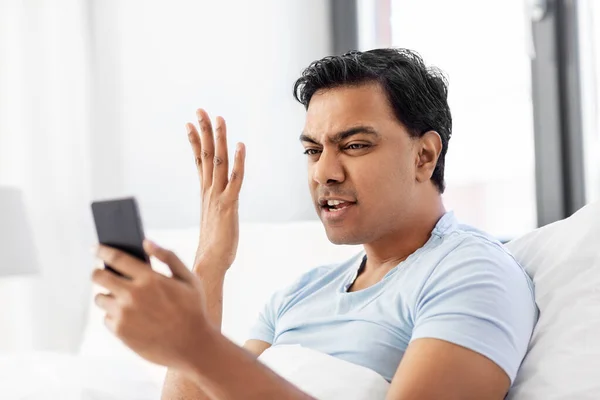 Indio enojado hombre con teléfono inteligente en la cama en casa —  Fotos de Stock