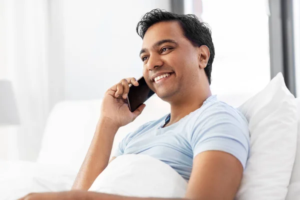 Hombre indio feliz llamando en el teléfono inteligente en la cama —  Fotos de Stock