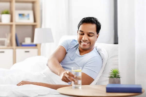幸せなインド人男性がベッドに横たわって水を飲む — ストック写真