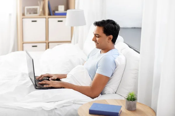 Homem indiano feliz com laptop na cama em casa — Fotografia de Stock