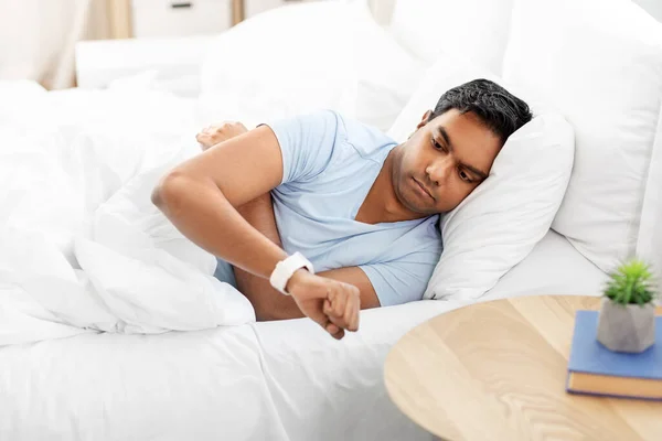 Indiaanse man op zoek naar slimme horloge in bed thuis — Stockfoto