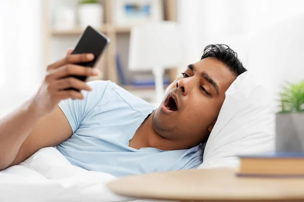 Hombre indio soñoliento con teléfono inteligente acostado en la cama —  Fotos de Stock