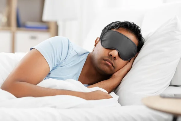 Индийский мужчина в маске для глаз спит в постели дома — стоковое фото