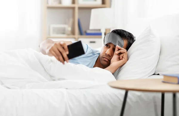 Hombre indio soñoliento con teléfono inteligente acostado en la cama — Foto de Stock