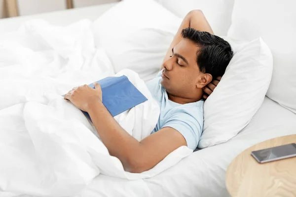 Indiana homem com livro dormindo na cama em casa — Fotografia de Stock