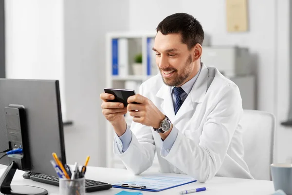 Médico varón sonriente con teléfono inteligente en el hospital — Foto de Stock