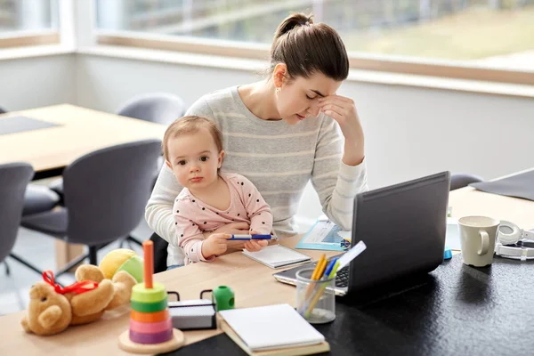 Втомлена мати з дитиною працює в домашньому офісі — стокове фото