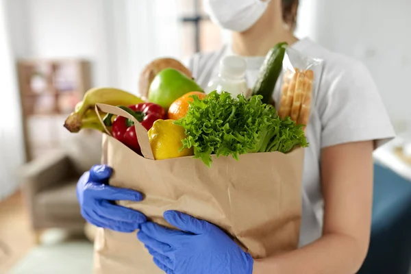 Mujer en guantes con comida en bolsa de papel en casa —  Fotos de Stock