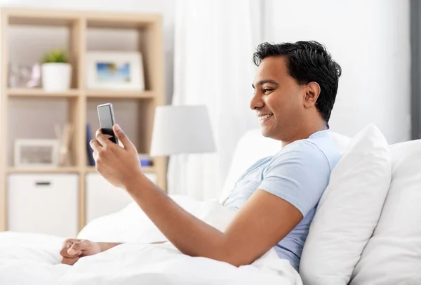 Hombre indio feliz con teléfono inteligente en la cama en casa — Foto de Stock