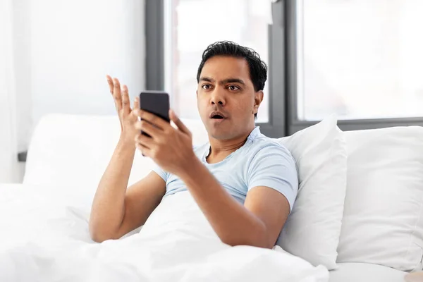 Indio enojado hombre con teléfono inteligente en la cama en casa — Foto de Stock