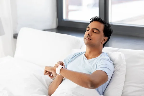 Homem indiano feliz com relógio inteligente na cama em casa — Fotografia de Stock