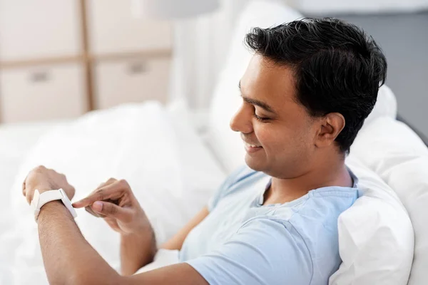 Hombre indio feliz con reloj inteligente en la cama en casa — Foto de Stock
