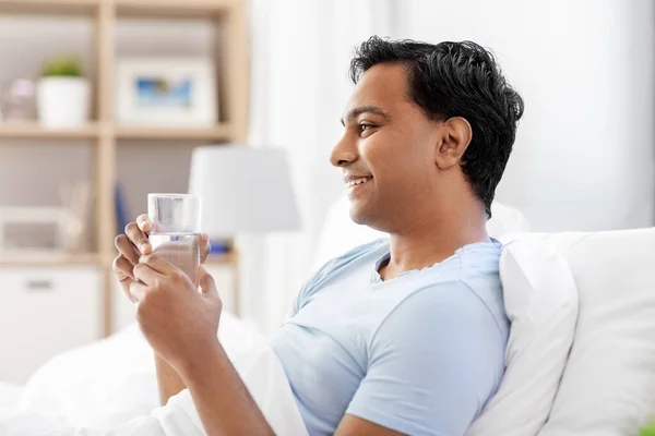 Hombre indio feliz beber agua acostado en la cama —  Fotos de Stock