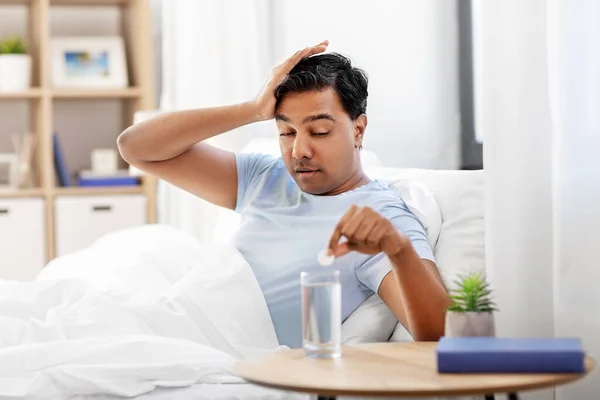 Beteg ember az ágyban gyógyszerrel és egy pohár vízzel. — Stock Fotó