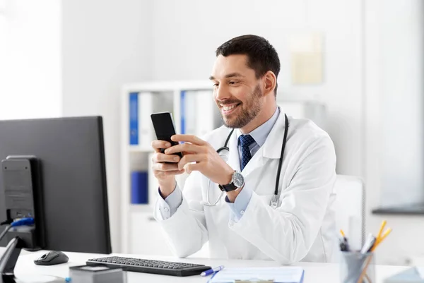 Sorridente médico masculino com smartphone no hospital — Fotografia de Stock