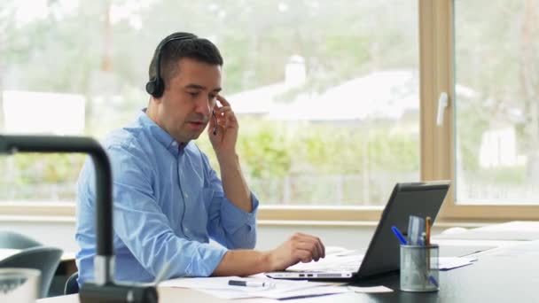 Hombre con auriculares y portátil trabajando en casa — Vídeos de Stock